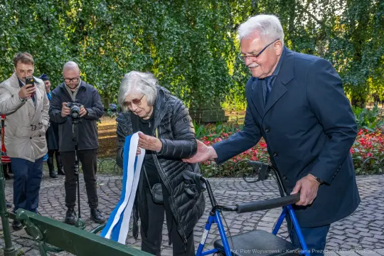 Uroczystość przecięcia wstęgi przez dwie osoby w parku.
