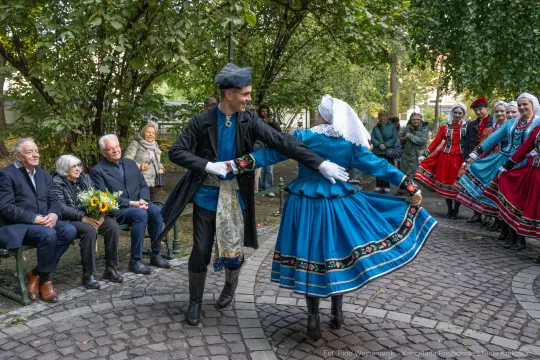 Tradycyjny taniec w strojach ludowych, widownia z uśmiechniętymi osobami.