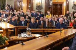 Zgromadzenie osób w sali obrad, w tym polityków i gości, podczas ważnego wydarzenia.