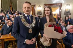 Mężczyzna w łańcuchu prezydenckim i kobieta z bukietem czerwonych róż w sali obrad.