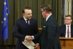 Dwaj mężczyźni uścisnęli sobie dłonie podczas ceremonii wręczenia dokumentu. W tle flaga Unii Europejskiej.