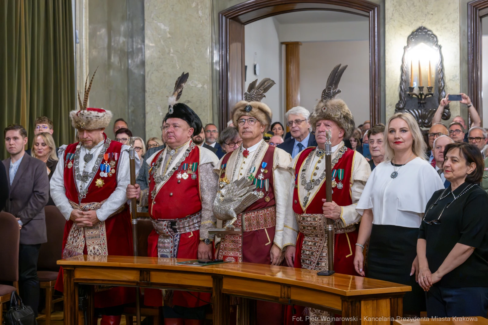 Mężczyźni w tradycyjnych strojach z odznaczeniami, stojący w sali z publicznością.  Autor: Piotr Wojnarowski