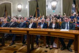 Grupa ludzi siedzących przy długim stole w sali z dekoracjami i oświetleniem.