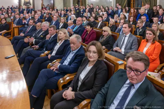 Zgromadzenie osób w sali, większość w garniturach, w tle widoczni goście i przedstawiciele władz.