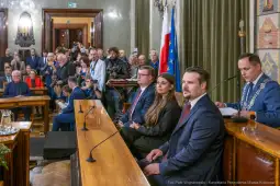 Sesja w sali obrad z uczestnikami i dziennikarzami, w tle flagi i przedstawiciele władz.