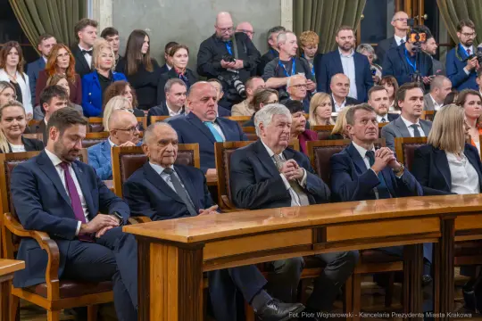Grupa ludzi w formalnych strojach siedzących przy stole w sali obrad.
