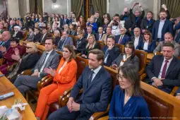 Spotkanie w sali obrad z uczestnikami i gośćmi, aplauz oraz różnorodne reakcje.