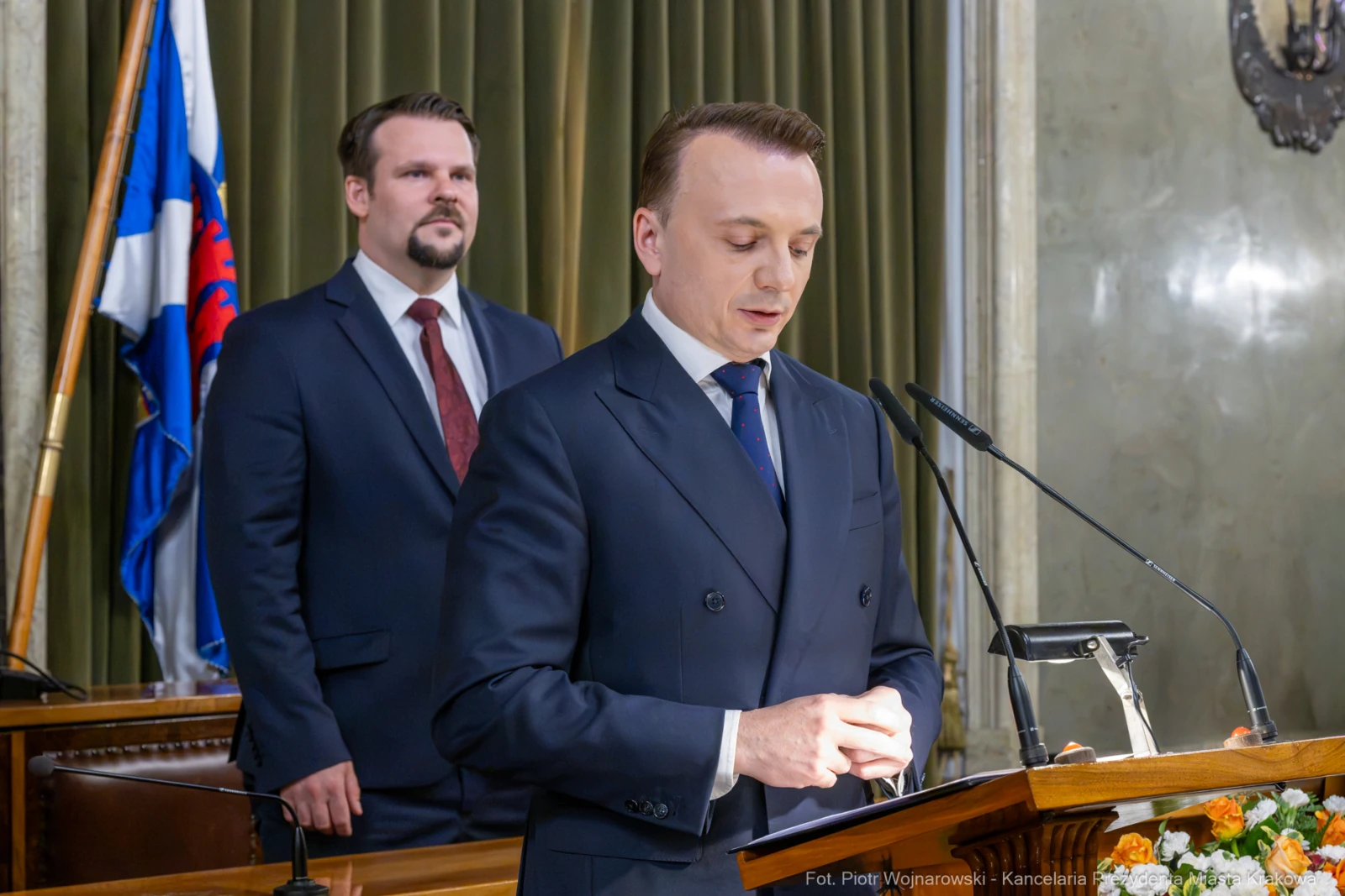 Mężczyzna przemawia z mównicy, w tle drugi mężczyzna w garniturze.  Autor: Piotr Wojnarowski