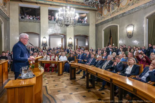 Wystąpienie mężczyzny przed zgromadzonymi gośćmi w eleganckiej sali.
