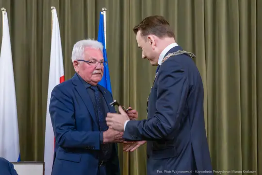 Dwóch mężczyzn w formalnych strojach, jeden z łańcuchem prezydenckim, wymieniający się dokumentami.