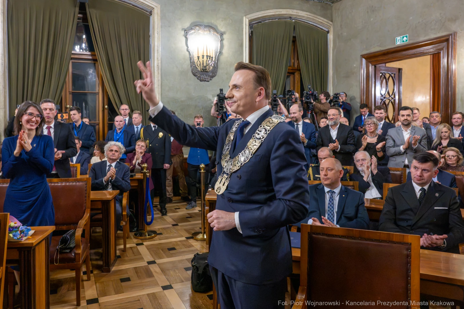 Mężczyzna w garniturze z łańcuchem na szyi wita zgromadzonych gości.  Autor: Piotr Wojnarowski