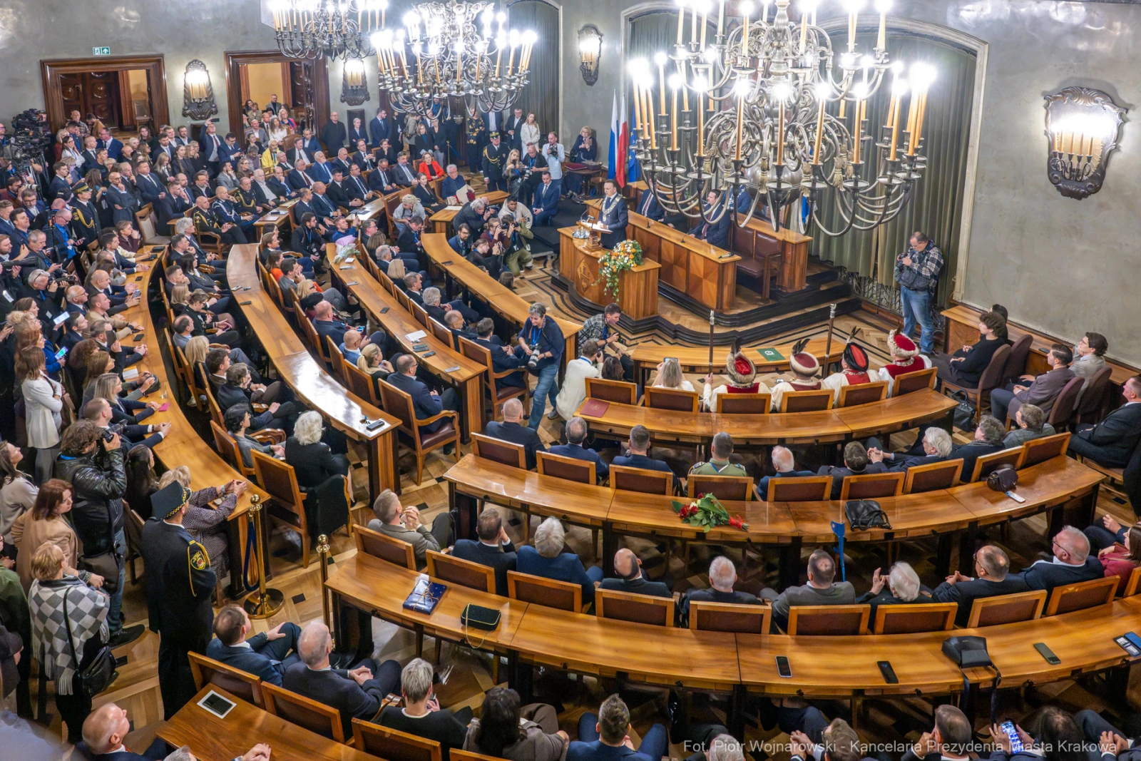 Zgromadzenie w sali obrad z mówcą na podium i uczestnikami w eleganckich strojach.  Autor: Piotr Wojnarowski