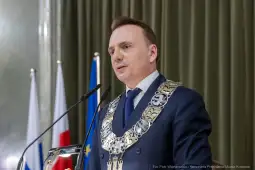Mężczyzna w garniturze z łańcuchem prezydenckim przemawia do zgromadzenia.