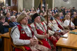 Mężczyźni w tradycyjnych strojach z insygniami, siedzący w sali obrad.