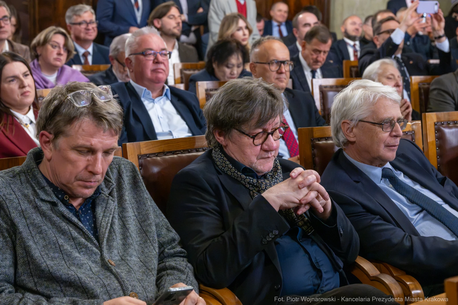 Grupa ludzi siedzących w sali, niektórzy z nich wpatrzeni w swoje telefony.  Autor: Piotr Wojnarowski