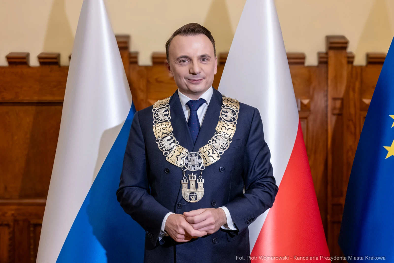 Mężczyzna w garniturze z łańcuchem prezydenckim, stojący między flagami Polski i Unii Europejskiej.  Autor: Piotr Wojnarowski