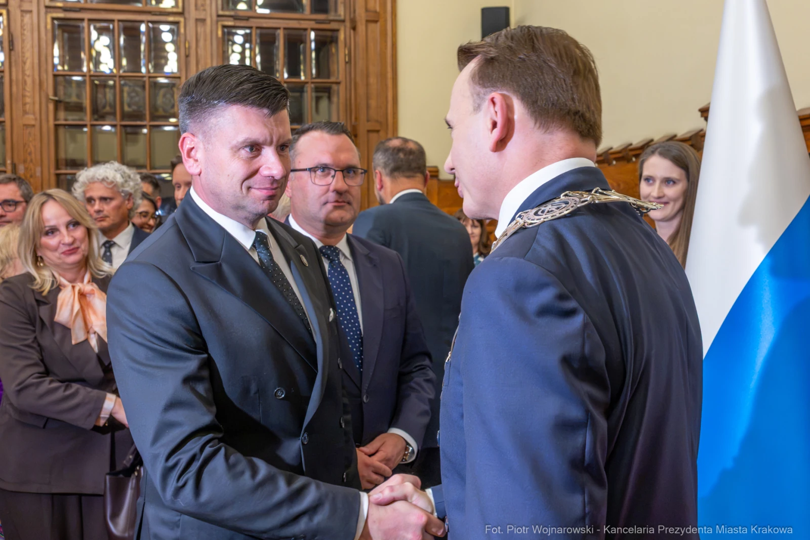 Spotkanie dwóch mężczyzn w garniturach, uściski dłoni, w tle goście i flagi.  Autor: Piotr Wojnarowski