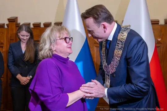Spotkanie dwóch osób, jedna w okularach, druga w łańcuchu honorowym. W tle inni uczestnicy.