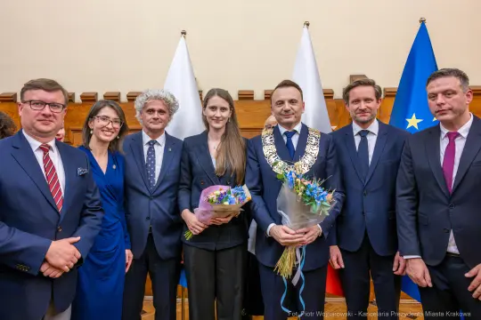 Uroczystość wręczenia nagród z udziałem kilku osób w garniturach i z kwiatami.