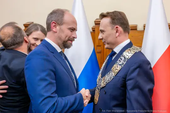 Dwaj mężczyźni w garniturach, jeden z łańcuchem prezydenckim, wymieniają uścisk dłoni.