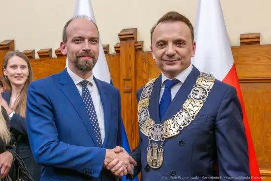 Dwaj mężczyźni uścisnęli sobie dłonie, w tle flagi Polski i Krakowa.