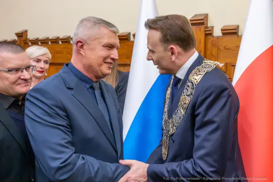Dwaj mężczyźni uścisnęli sobie dłonie, w tle flagi Polski i innego kraju.