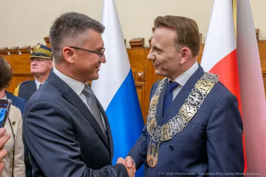 Dwaj mężczyźni uścisnęli sobie dłonie, w tle flagi Polski i Rosji.
