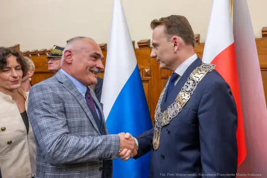 Mężczyźni w garniturach uścisną ręce, w tle flagi Polski i Rosji.