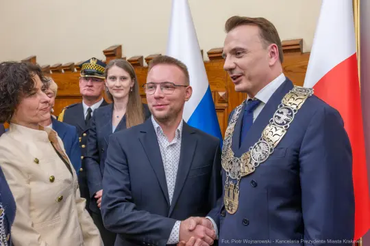 Spotkanie dwóch mężczyzn w garniturach, jeden z łańcuchem prezydenckim, w otoczeniu innych osób.