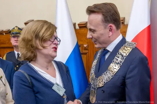 Spotkanie dwóch osób, jedna z nich w łańcuchu prezydenckim, w tle flagi.
