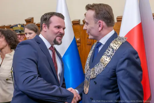 Mężczyźni w garniturach uścisną ręce, w tle flagi Polski i Rosji.