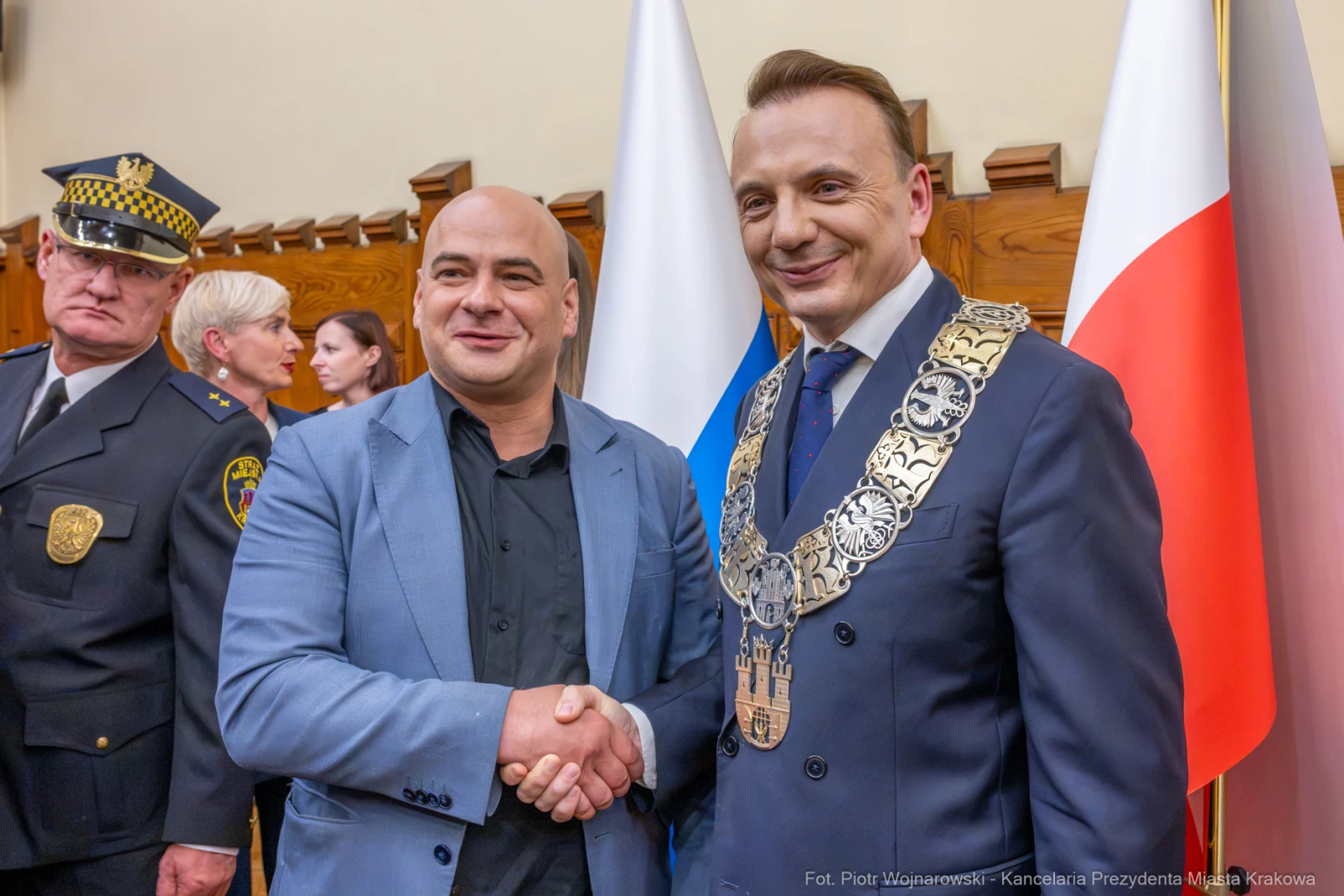 Dwaj mężczyźni uścisnęli sobie dłonie, w tle flagi i osoby w garniturach.  Autor: Piotr Wojnarowski