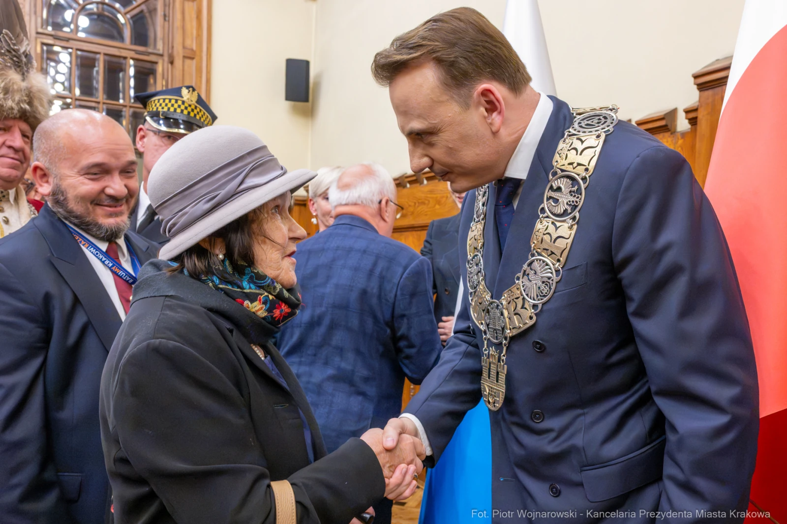 Spotkanie dwóch osób, jedna z nich w kapeluszu, uściski dłoni, w tle inni uczestnicy wydarzenia.  Autor: Piotr Wojnarowski