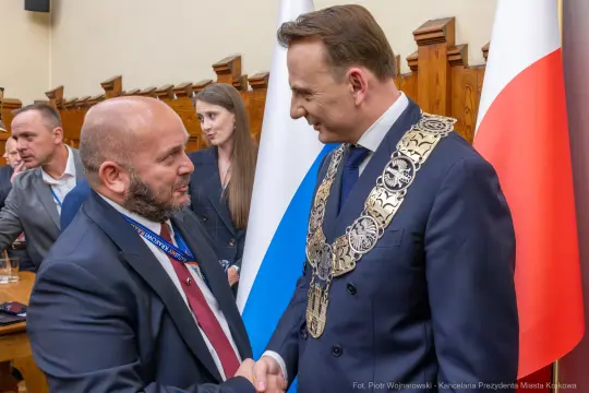 Dwaj mężczyźni uścisnęli sobie dłonie, w tle flagi Polski i Krakowa.