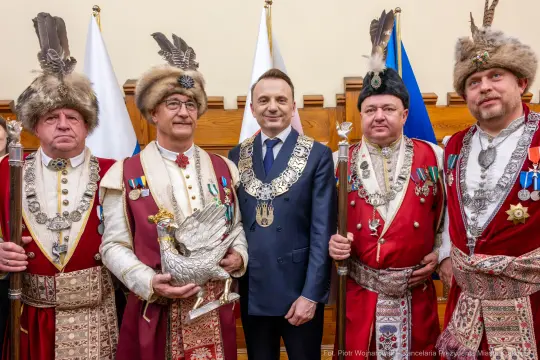 Mężczyźni w tradycyjnych strojach, z odznaczeniami, pozują z symbolem orła.