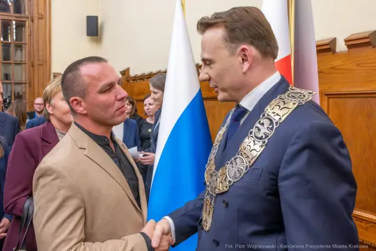 Spotkanie dwóch mężczyzn, jeden w garniturze, drugi w jasnej marynarce, uścisk dłoni.