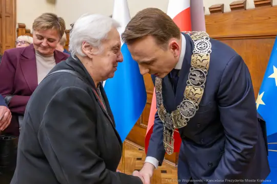 Spotkanie dwóch osób, jedna z nich w łańcuchu prezydenckim, w tle flagi Polski i Unii Europejskiej.