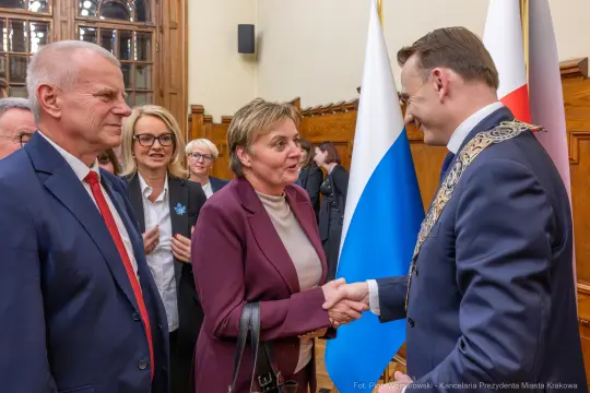 Spotkanie przedstawicieli władz z uściskiem dłoni. Flagi Polski i Krakowa w tle.