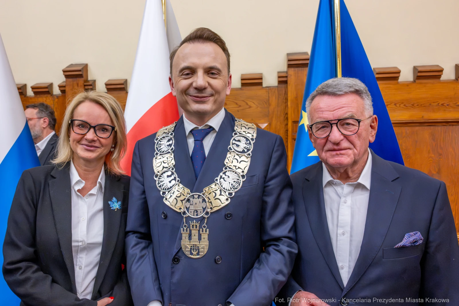 Nowy prezydent Krakowa w towarzystwie dwóch osób, z flagami w tle.  Autor: Piotr Wojnarowski