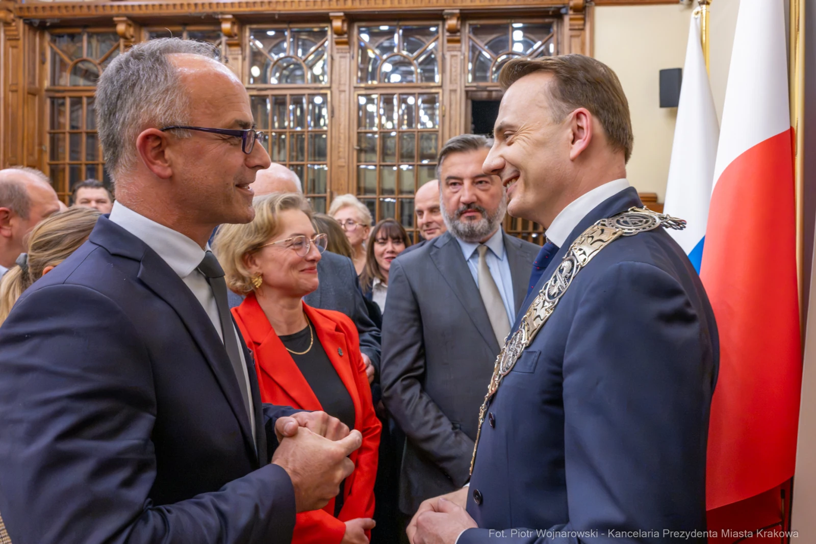 Spotkanie dwóch mężczyzn w formalnych strojach, w tle flagi i goście w eleganckich ubraniach.  Autor: Piotr Wojnarowski