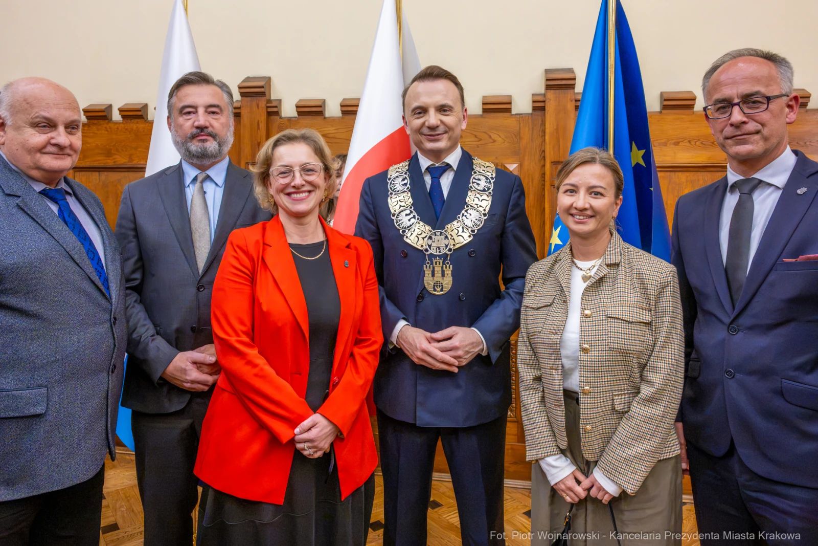 Grupa ludzi w formalnych strojach, w tym prezydent, na tle flag i emblematu.  Autor: Piotr Wojnarowski