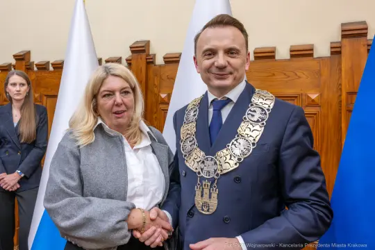 Spotkanie dwóch osób, jedna z nich w łańcuchu prezydenckim, w tle flagi.