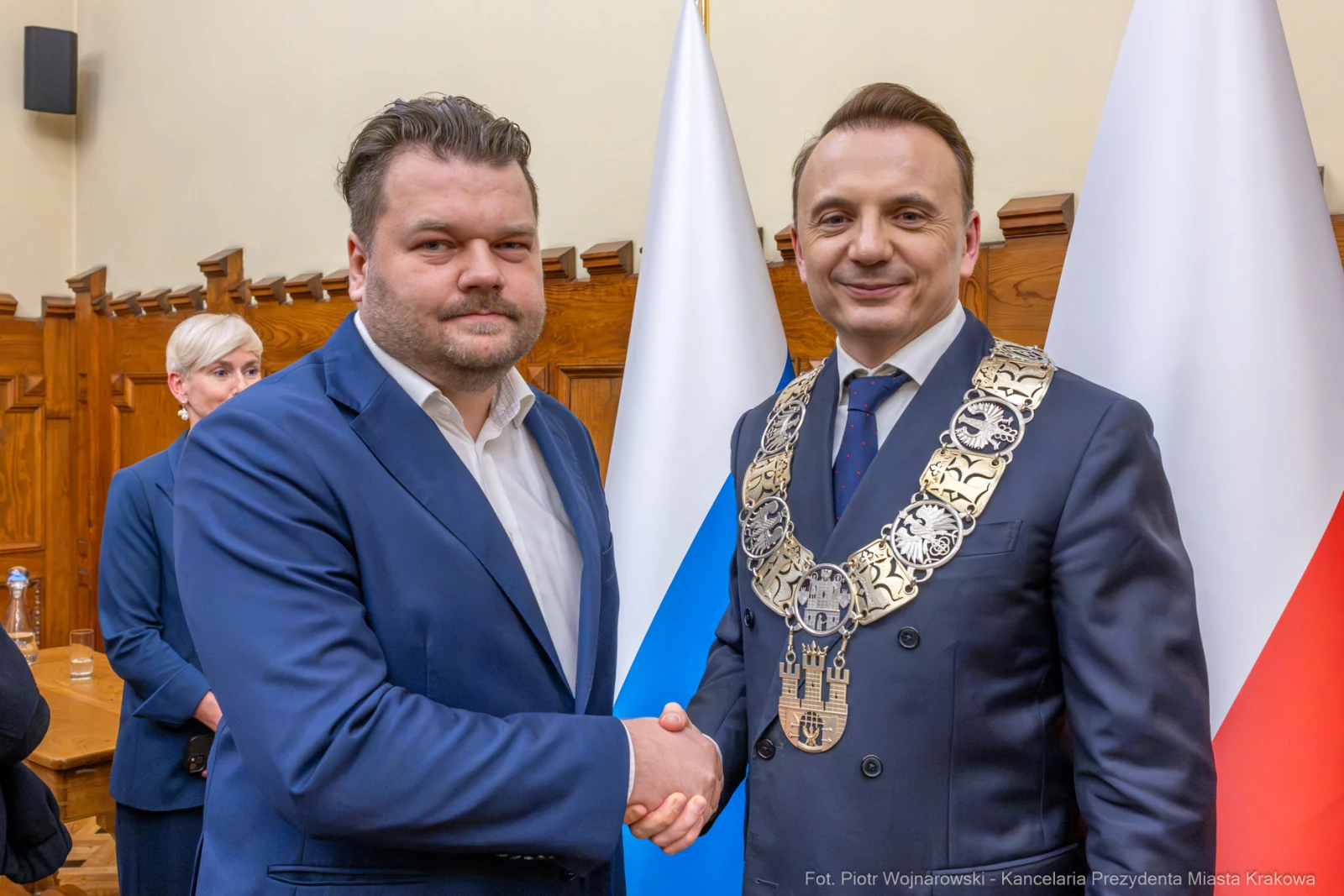 Dwóch mężczyzn w garniturach uścisnęło sobie dłonie, w tle flagi Polski i Krakowa.  Autor: Piotr Wojnarowski