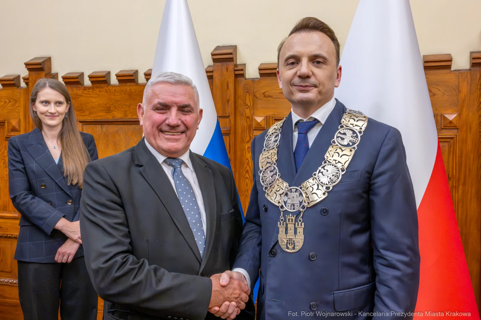 Dwóch mężczyzn w garniturach uścisnęło sobie dłonie, w tle flagi. Kobieta stoi z boku.  Autor: Piotr Wojnarowski