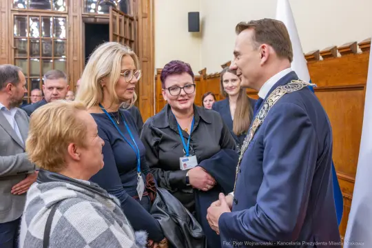 Spotkanie grupy ludzi z mężczyzną w oficjalnym stroju, rozmowy i uśmiechy.