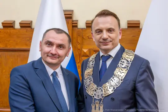 Dwaj mężczyźni w garniturach, jeden z łańcuchem prezydenckim, stoją obok siebie.