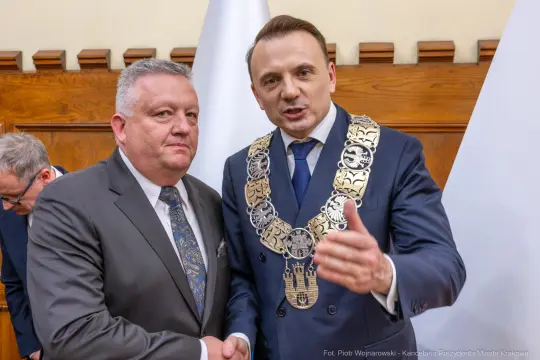 Dwóch mężczyzn w garniturach, jeden z łańcuchem prezydenckim, w tle flagi.