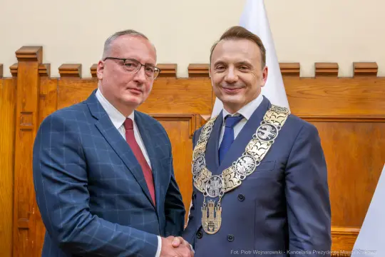 Dwaj mężczyźni w garniturach, jeden z łańcuchem prezydenckim, uściski dłoni.