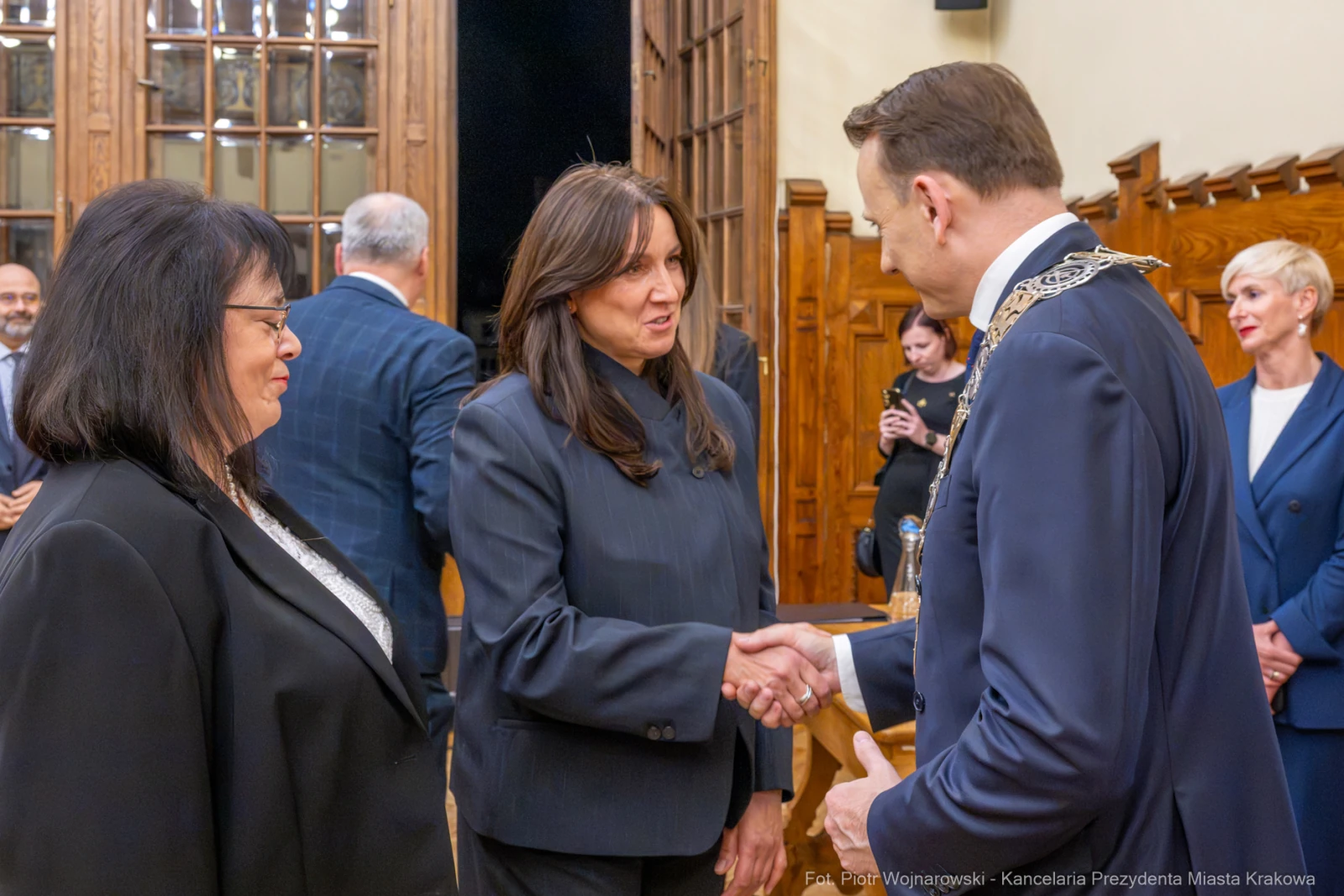 Spotkanie dwóch osób w formalnych strojach, uścisk dłoni, w tle inni uczestnicy wydarzenia.  Autor: Piotr Wojnarowski