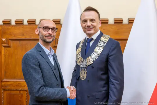 Dwóch mężczyzn w garniturach, jeden z łańcuchem prezydenckim, uściski dłoni.